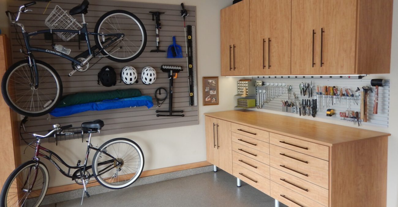 Warm wood-toned garage storage with bikes mounted on slat wall panels and cabinetry organizing helmets, tools, and accessories.