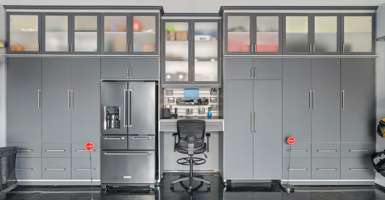 Sophisticated gray garage cabinetry system with a refrigerator, overhead frosted glass cabinets, and a central workstation