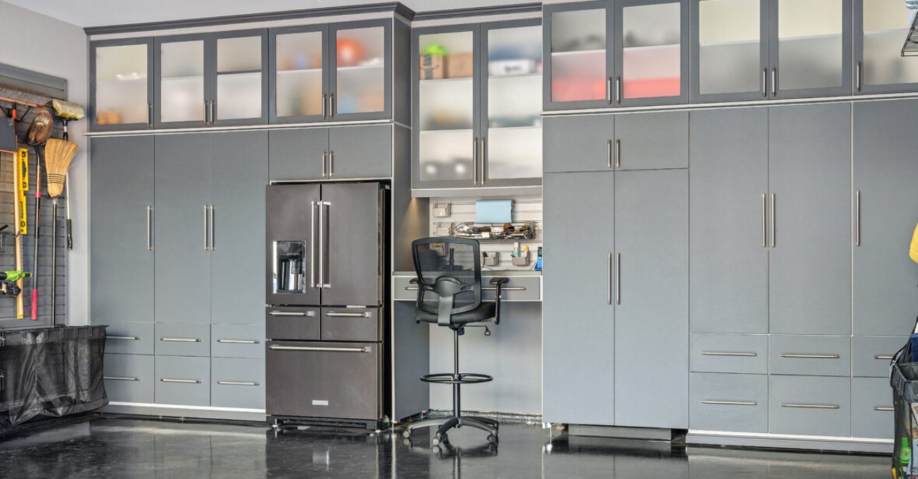 Gray garage built-in setup with an integrated refrigerator, tool workstation, and high cabinets for concealed storage.