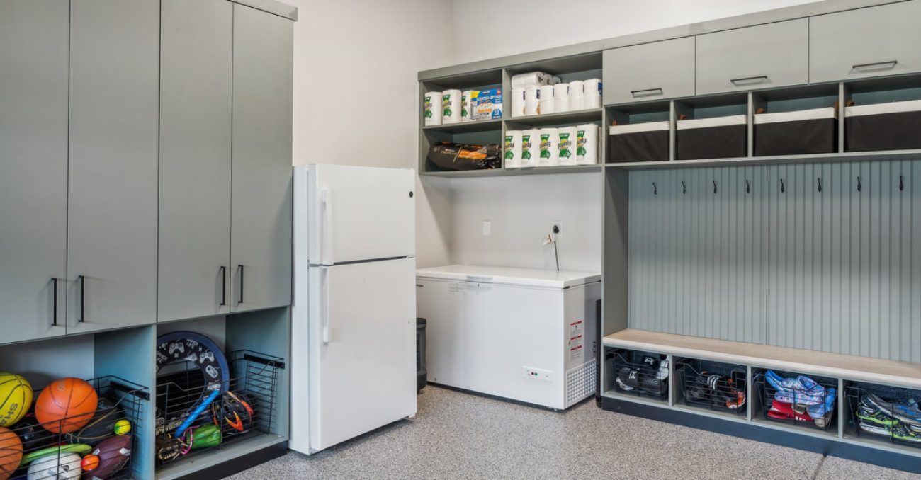 Gray mudroom-style garage design with full-height cabinets, wire baskets, overhead cubbies, and bench seating