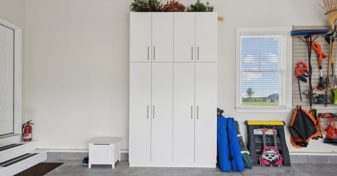 Garage with white cabinetry with integrated handles, slatwall system for garden tools and power equipment