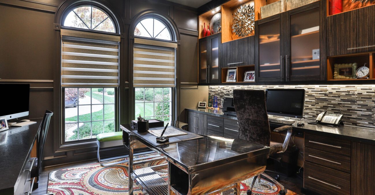Sophisticated home office with dark wood cabinetry, metallic backsplash, under-cabinet lighting, and built-in cubbies for organized storage.