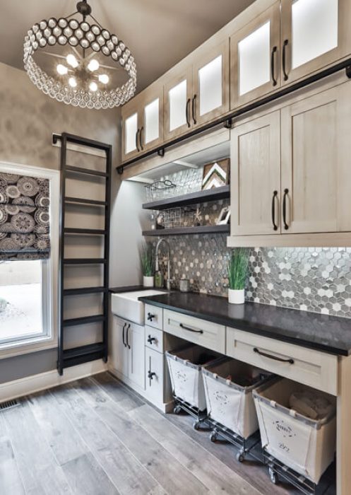 Elegant mudroom with upper glass-front cabinets, rolling ladder, mosaic tile backsplash, built-in laundry hampers, and shaker-style cabinetry.