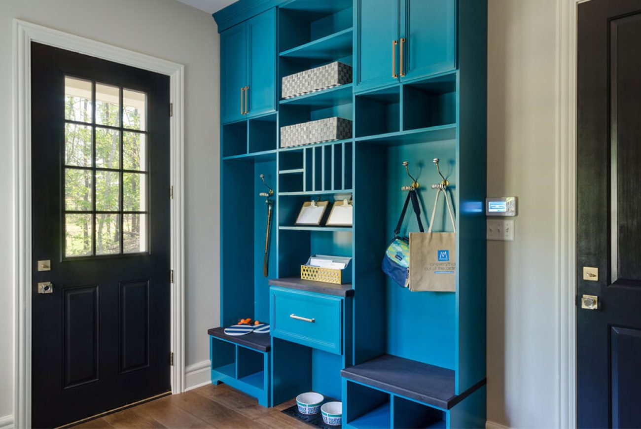 Mudroom with floor-to-ceiling teal cabinetry, featuring cubbies, hooks, built-in seating, and organized storage baskets.