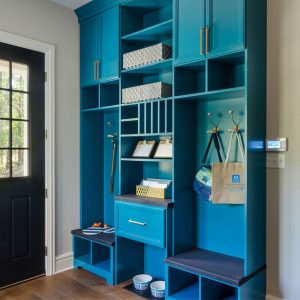 Mudroom with floor-to-ceiling teal cabinetry, featuring cubbies, hooks, built-in seating, and organized storage baskets.