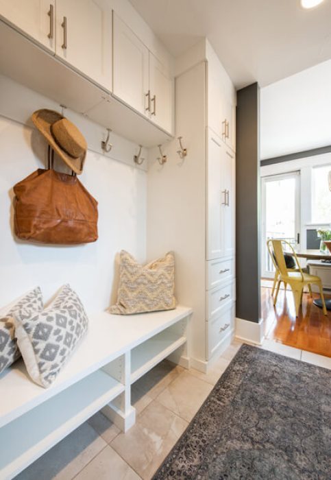 White mudroom built-in with hooks, a bench with pillows, upper cabinets, and a side drawer tower