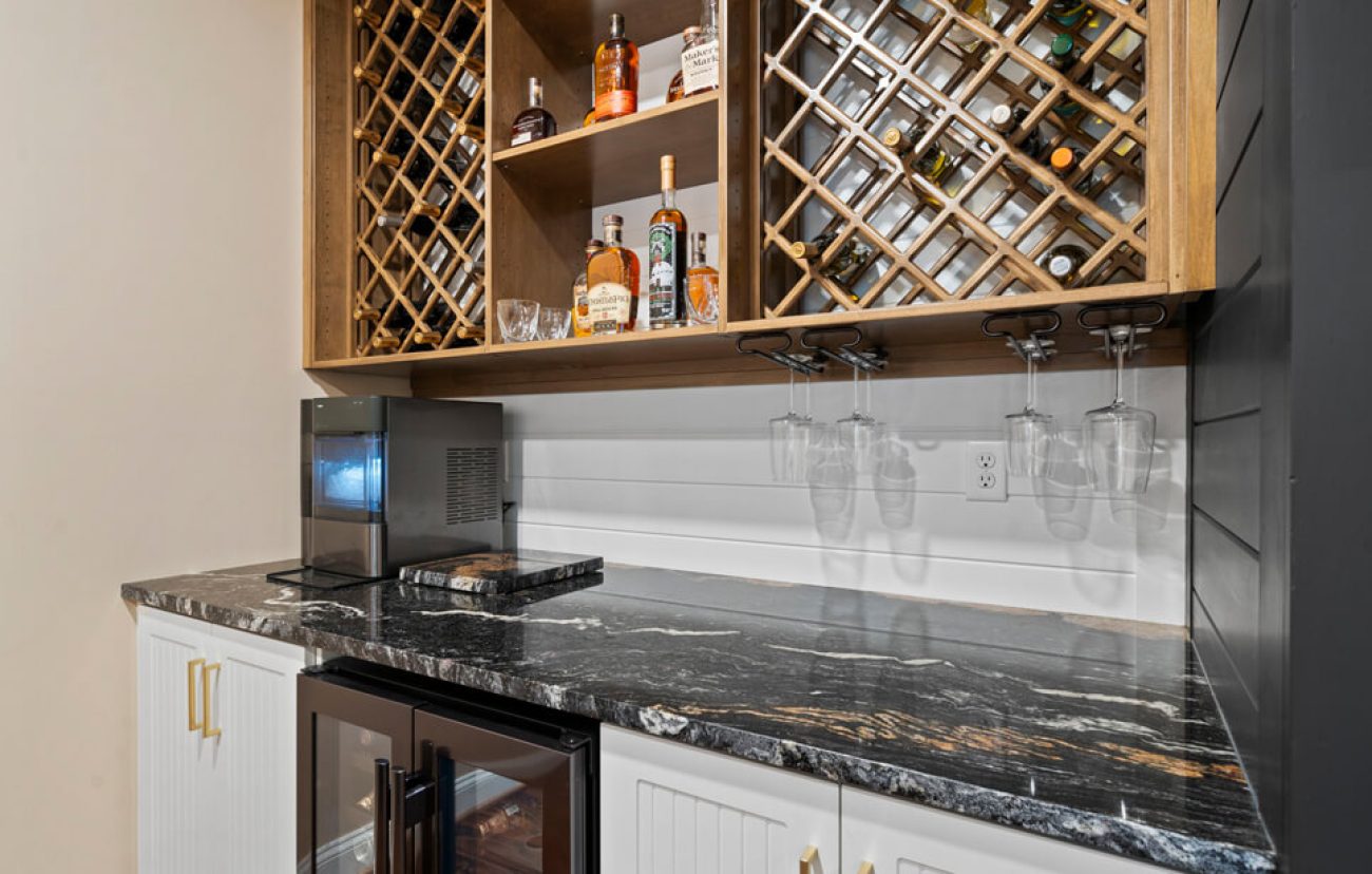 Wet bar with dark granite countertop, undercabinet wine fridge, stemware holders, and wooden lattice-style wine racks.