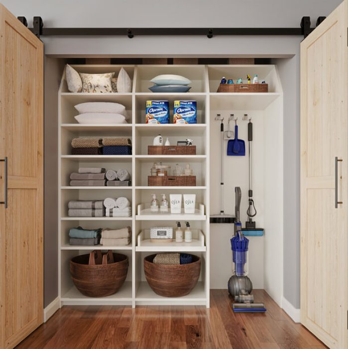 Multi-use storage closet with white cubbies, woven baskets, towel stacks, and built-in hanging space for vacuum and cleaning supplies.