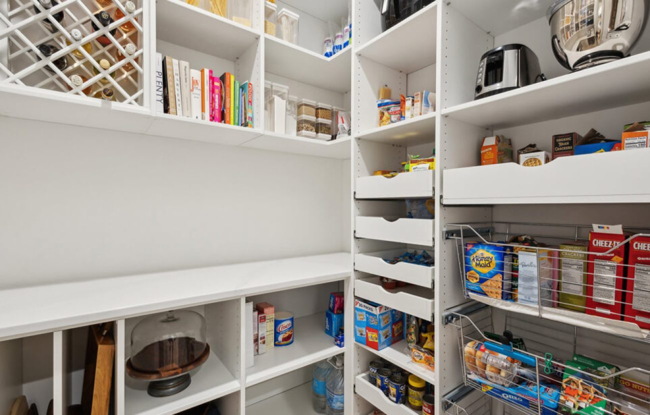 Organized white pantry with wine bottle storage, pull-out drawers, wire baskets, cookbooks, and countertop appliances.