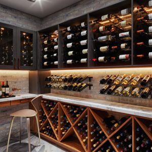 Modern wine room with black shelving, exposed brick walls, under-cabinet lighting, and marble countertops, displaying an extensive wine collection and glassware.