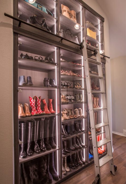 Custom shoe shelving display with glass fronts and LED lighting strips, accompanied by rolling ladder for access to high shelves