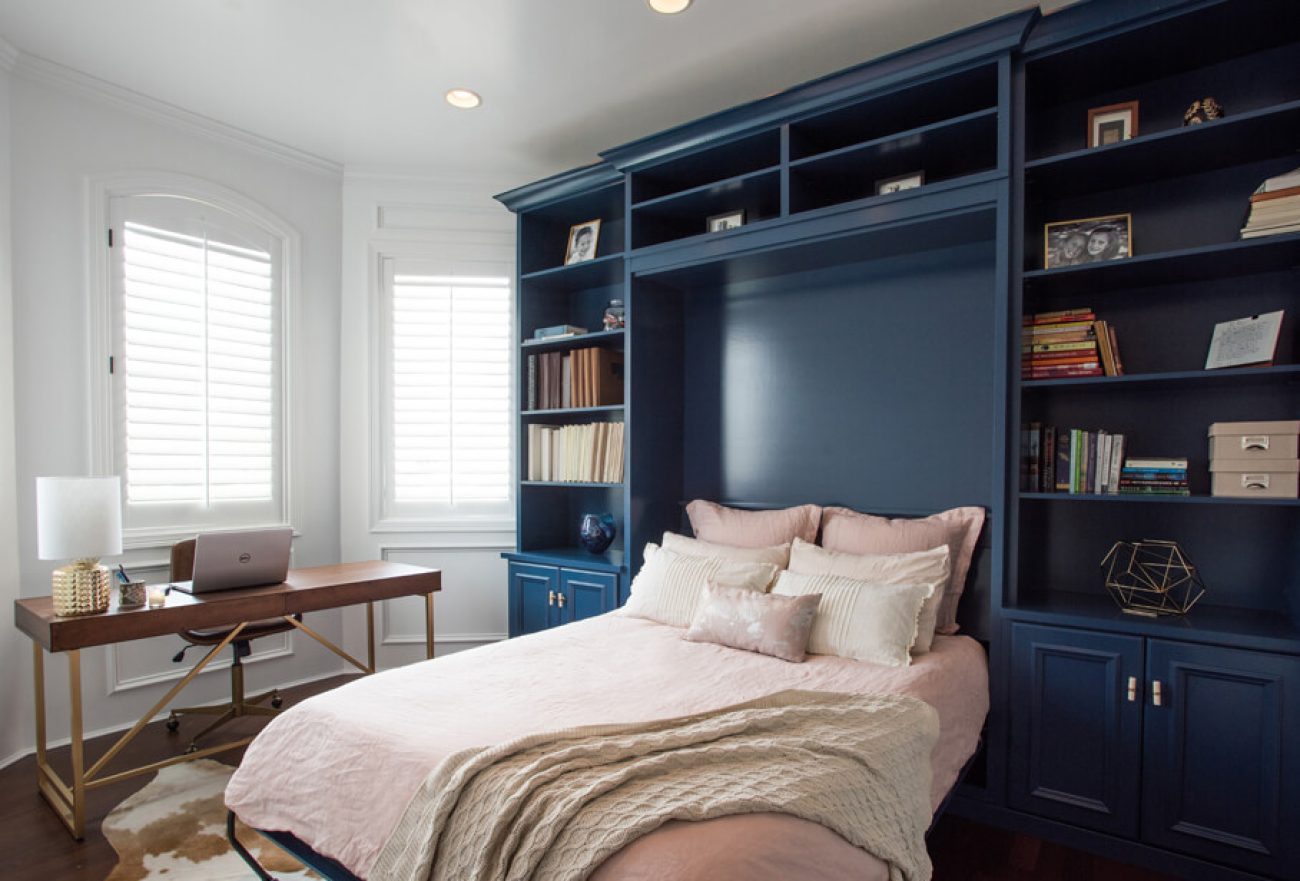Navy blue built-in wall bed with surrounding bookcases and upper storage