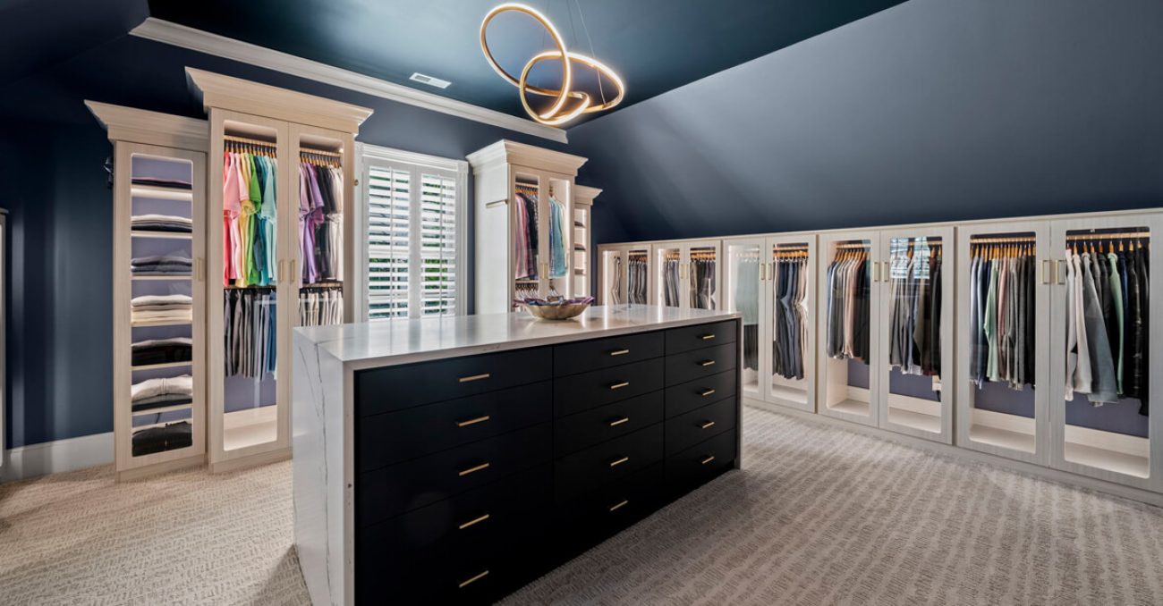 Wardrobe closet with all glass door fronts and black central island with flat front door faces and waterfall edge marble countertop.
