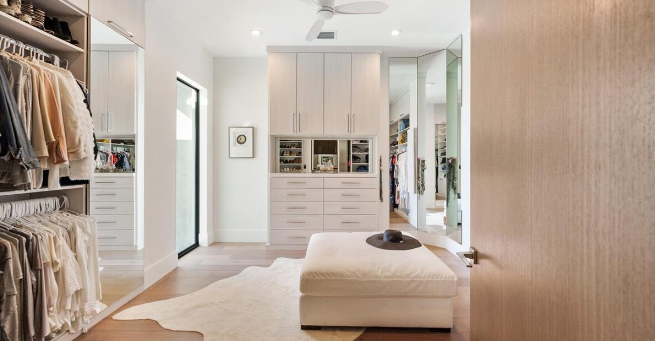 Contemporary wardrobe closet with slab front cabinet doors and drawers. The central built-in unit features mirrored cubbies with velvet-lined necklace organizers.