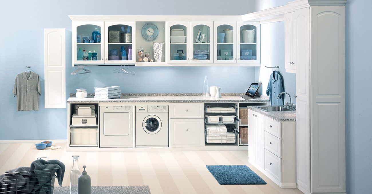 Custom laundry room cabinetry with glass door fronts, pull-out wire baskets, hanging rods, integrated laundry sink, and folding station.