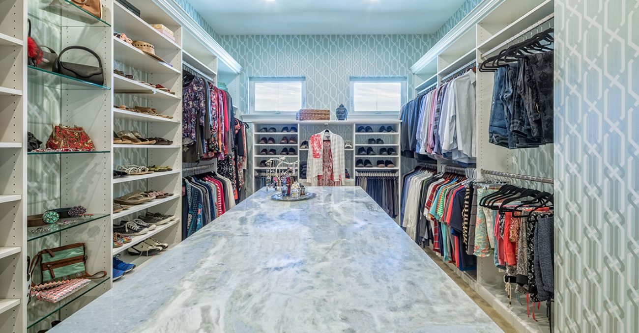 Large central island and dual handing rods in walk-in closet. Features glass open shelving and crown molding.