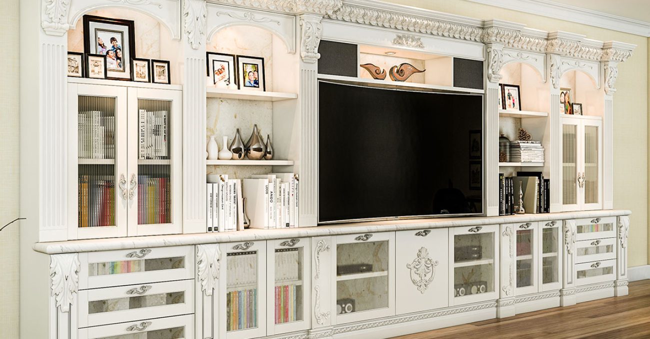 Traditional white entertainment center with ornate crown molding, fluted pilasters, built-in shelving, and glass cabinet doors.