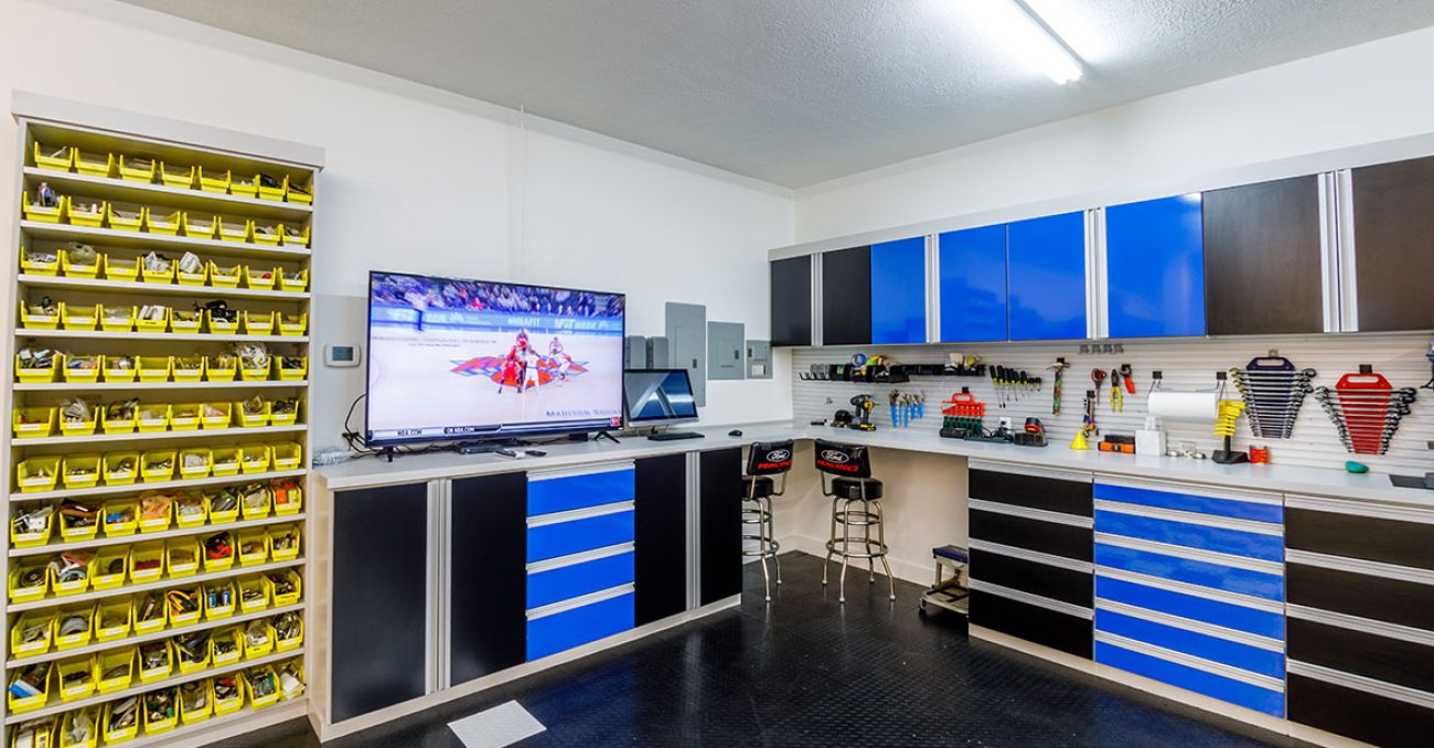 Man cave & garage combination with open shelving unit, slatwall tool storage, high gloss dual-tone cabinetry and drawers with sleek metallic pulls.