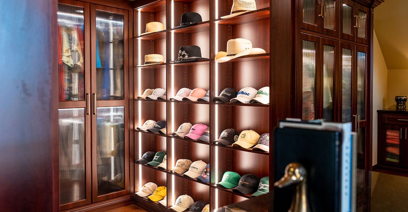 Sophisticated wardrobe suite with floor-to-ceiling fluted glass doors, wraparound cabinetry, and built-in hat display shelving with integrated lighting.