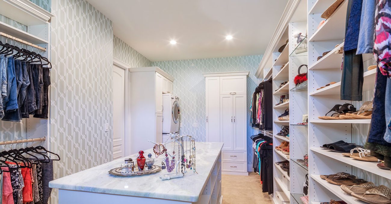 Stacked washer & dryer inside walk-in closet with custom cabinetry and shelving.