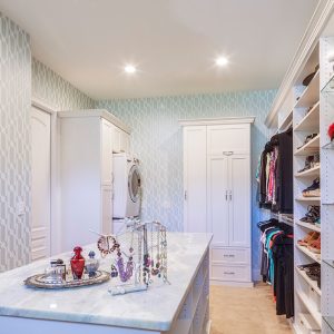 Stacked washer & dryer inside walk-in closet with custom cabinetry and shelving.