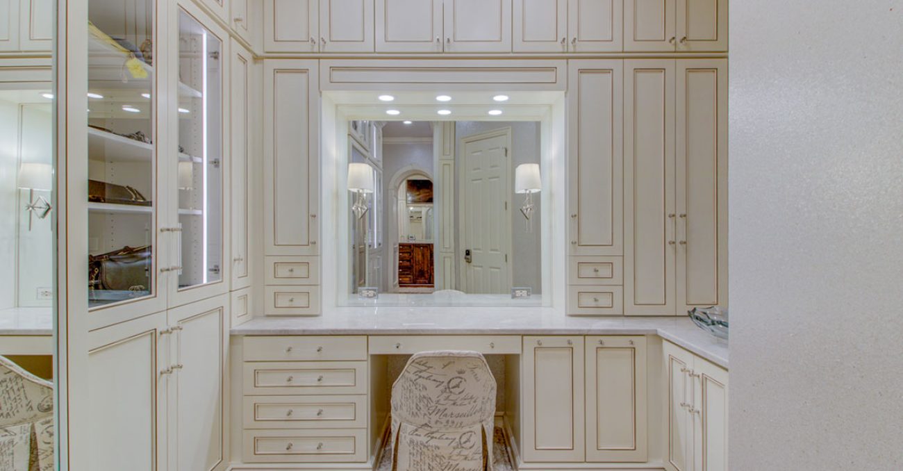 Full vanity suite built into a dressing room with glass insert cabinet doors and integrated lighting surrounding mirror.