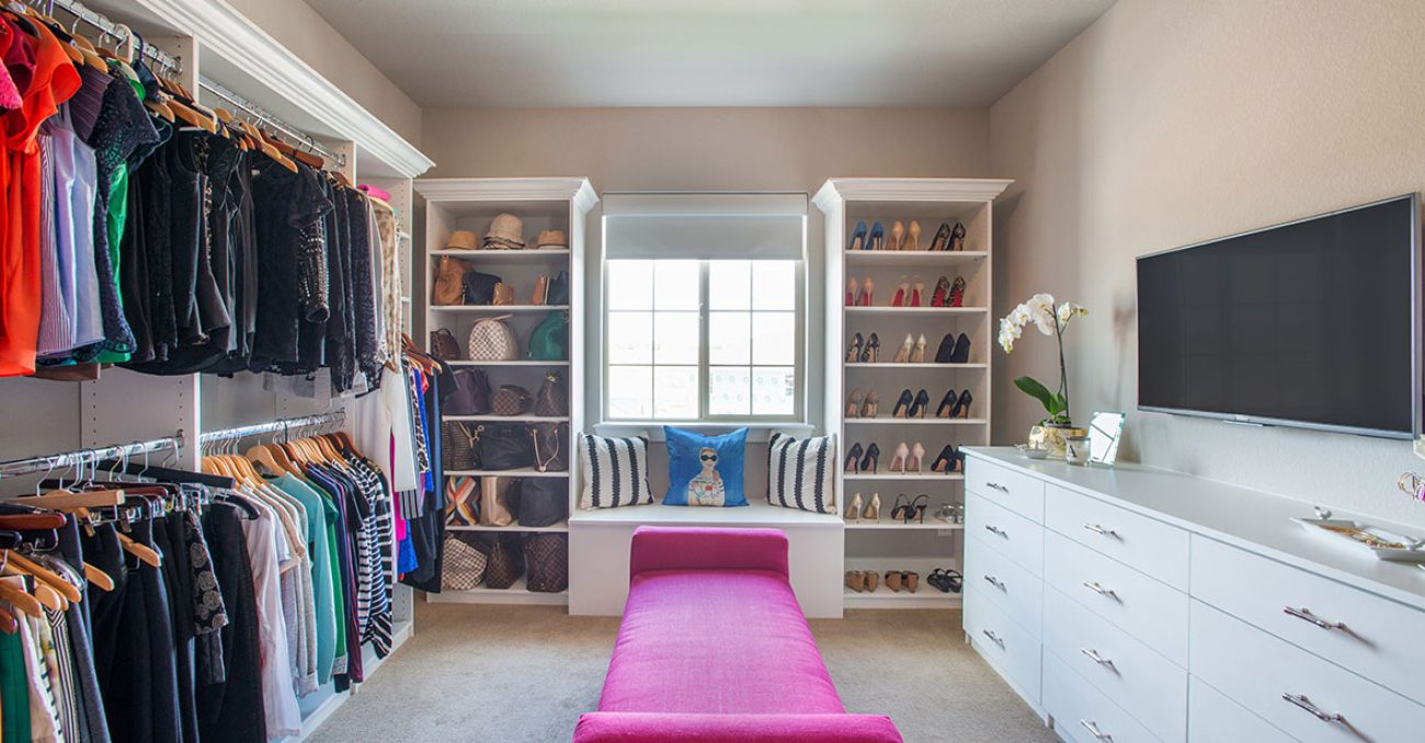 Walk-in closet with dual hanging rods, crown molding, built-in drawers and window seat bench.