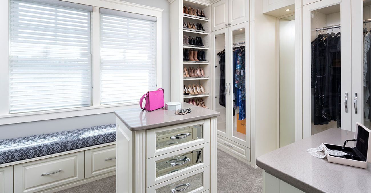 Walk-in closet with open shoe shelving with elite chrome toe stops, glass inset door fronts, and integrated window bench.
